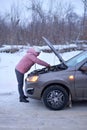 Car repair on the road in winter. young girl is trying to fix a car breakdown under the soot on the road. woodsroadside assistance Royalty Free Stock Photo