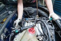 A car repairman unscrews parts with a wrench with a green handle in the engine compartment suh as spark plugs and ignition coils