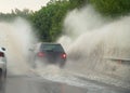 Car runs into big puddle at heavy rain, water splashing over the car. Car driving on asphalt road at thunder storm. Dangerous driv Royalty Free Stock Photo