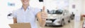 Car sales manager holds thumbs up in car dealership