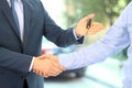 Car salesman handing over the keys for a new car to a young businessman . Handshake between two business people. Focus on a key