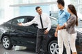 Car Salesman Invites Customers at Showroom. Royalty Free Stock Photo
