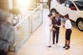 Car salesman standing at dealership telling about features of car to customers Royalty Free Stock Photo