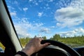 Car salon, steering wheel, hand of woman and view on nature landscape. Road, forest, blue sky, white clouds at sunny day. Concept Royalty Free Stock Photo