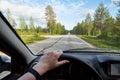 Car salon, steering wheel, hand of woman and view on nature landscape. Road, forest, blue sky, white clouds at sunny day. Concept Royalty Free Stock Photo