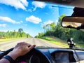 Car salon, steering wheel, hand of woman and view on nature landscape. View from seat of driver on Road, forest, blue