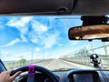 Car salon, steering wheel, hand of woman and view on nature landscape. View from seat of driver on Road, forest, blue