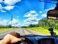 Car salon, steering wheel, hand of woman and view on nature landscape. View from seat of driver on Road, forest, blue