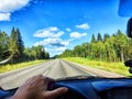 Car salon, steering wheel, hand of woman and view on nature landscape. View from seat of driver on Road, forest, blue