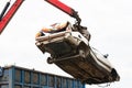 Car in a scrap yard being lifted by a mechanical grabber crane to be scrapped