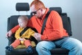 Car seat belt. A happy child is sitting in auto armchair next to man with red hair, beard and mustache in yellow shirt, glasses wi Royalty Free Stock Photo