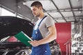 Car service, repair, maintenance and people concept - auto mechanic man or smith with clipboard at workshop Royalty Free Stock Photo