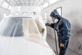 Car service station. Worker painting a white car in special garage, wearing costume and protective gear Royalty Free Stock Photo