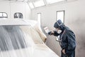 Car service station. Worker painting a white car in special garage, wearing costume and protective gear Royalty Free Stock Photo