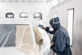 Car service station. Worker painting a white car in special garage, wearing costume and protective gear Royalty Free Stock Photo