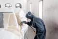 Car service station. Worker painting a white car in special garage, wearing costume and protective gear Royalty Free Stock Photo