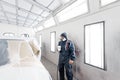 Car service station. Worker painting a white car in special garage, wearing costume and protective gear Royalty Free Stock Photo