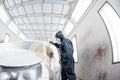 Car service station. Worker painting a white car in special garage, wearing costume and protective gear Royalty Free Stock Photo