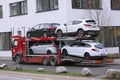 Car shipping auto transport vehicle with cars loaded driving in front of office buildings