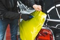 a car specialist wrapping neon yellow vinyl film on a black car at the repair shop