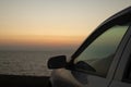 The car is standing over a cliff by the sea. The sunset rays of the sun are reflected in the glass. Pink and orange tones create