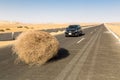 A car stopped by a giant tumbleweed on a highway with sandy dunes, between Bahariya oasis and Farafra, Western Desert of Egypt.