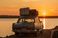 car, with suitcases on the roof, driving past lake during sunset