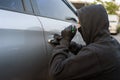 A car thief wears black gloves and holds a screwdriver to pry open the car door