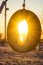 Car tire swing on sunset. Rubber wheel on the rope in the winter evening sun rays. Warm sunset on the kids playground