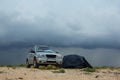 Car and touristic tent on a sandy beach under a bense rainy cloudy sky