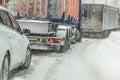 Car waiting behind large trucks during traffic jam on forest road, caused by heavy snow blizzard