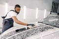 Car wash and clean with shampoo and sponge. Young concentrated African American man worker, wearing gray overalls and Royalty Free Stock Photo