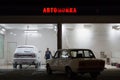 A car wash on the night highway - one car is in foam, another is standing nearby, in the center is a man - worker in a blue T-