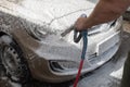 Car wash, white soap foam flies from the pump to the hood and headlight of the car, car washer at work