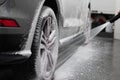 Car wash worker spraying car wheel and tire with white active cleaning foam Royalty Free Stock Photo