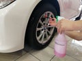A car wash worker washes a car disk with a brush and holds a spray bottle with auto chemistry.