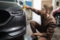 Side view of caucasian man worker of car wash service cleaning headlights of luxury grey car Royalty Free Stock Photo