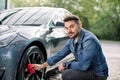 Car washing on open air. Young bearded man cleaning a wheel, car rims of modern luxury gray electric car with red Royalty Free Stock Photo