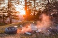 A car wheel next to a heap of burning junk in the forest