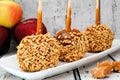 Caramel apples with nuts on a plate against white wood