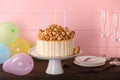 Caramel drip cake decorated with popcorn and pretzels near balloons and tableware on wooden table Royalty Free Stock Photo