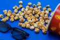 Caramel popcorn scattered on a blue background and 3D glasses for watching a movie. The concept of the film. Food for watching