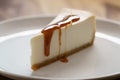 Caramel sauce poured on slice of traditional new york cheesecake on white plate on wood table