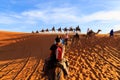 Caravan of camels with tourist in the desert at sunset