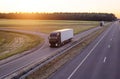 A caravan of modern freight trucks transports cargo in the evening against the sunset. Trucks drive on the motorway in