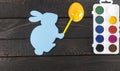 Card bunny with marker on it`s hand, painting egg into yellow on dark brown wooden background. Royalty Free Stock Photo