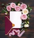 Card and envelope between pink and cream roses on brown wood top view, wedding mockup Royalty Free Stock Photo