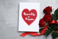 Card with love message near red roses on grey table, flat lay Royalty Free Stock Photo