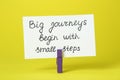 Card with phrase Big Journeys Begin With Small Steps and clothespin on yellow background. Motivational quote Royalty Free Stock Photo