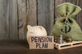 Card with phrase Pension Plan, stacks of coins, piggy bank and sack on wooden table. Retirement concept